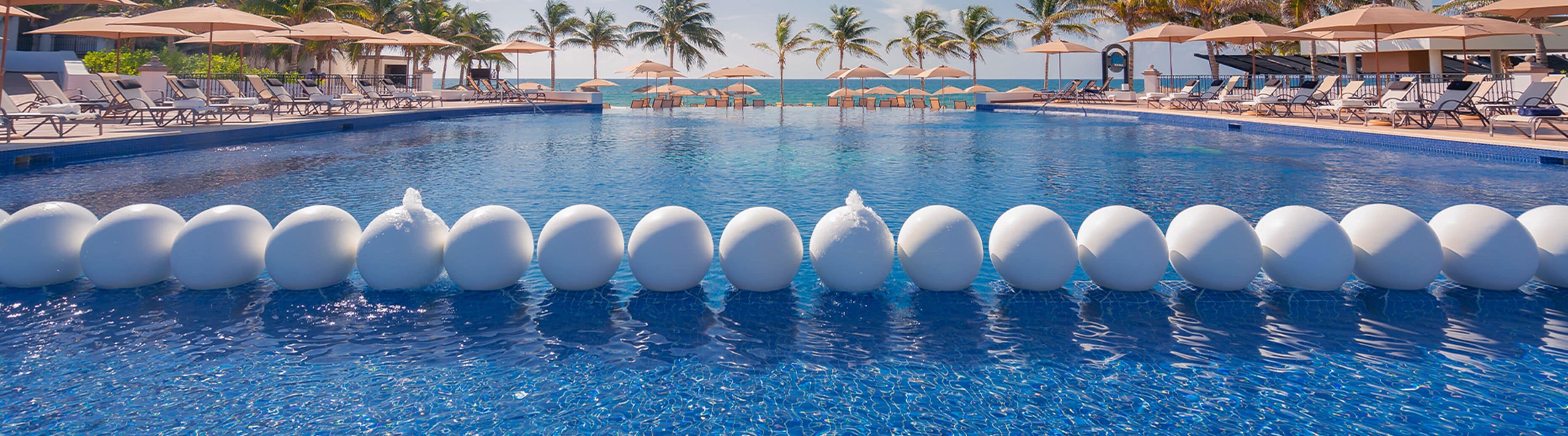 Une piscine où flottent des sphères blanches à la surface de l’eau, entourée de chaises longues et de parasols.