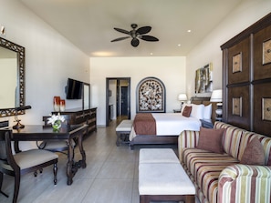 A hotel room with a bed, a sofa, a desk with a chair, a television, and a ceiling fan.