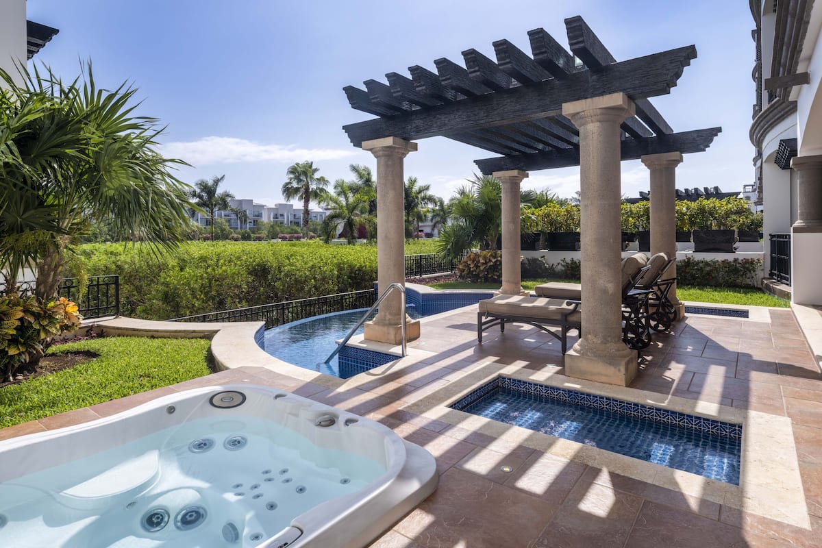 A pool area with a hot tub, lounge chairs, and a pergola.