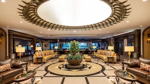 A lobby with a central circular seating area, a large tree planter, and a bar in the background. - Holiday Inn Club Vacations Grand Residences by IHG - All Inclusive (Puerto Morelos)