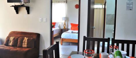 A hotel room with a TV mounted on the wall, a dining table set with plates, glasses, and a bowl of flowers.