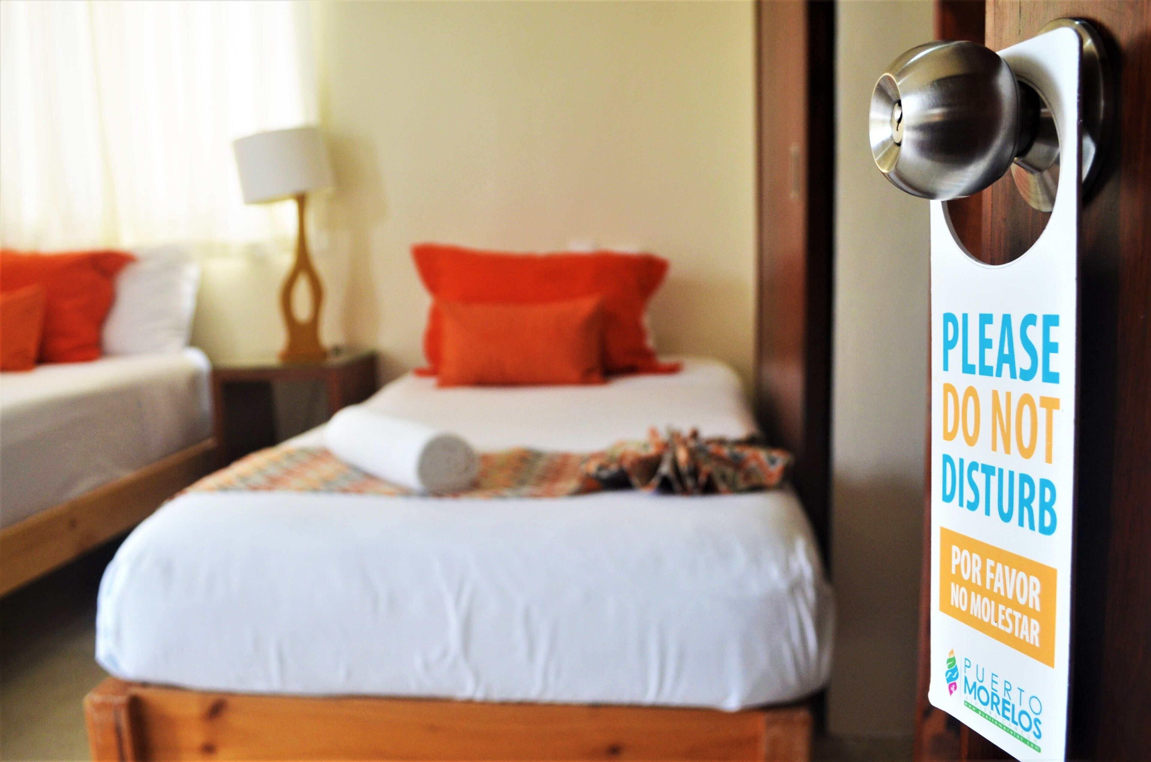 Una habitación de hotel con cama, almohadas, una lámpara y un cartel en la puerta.