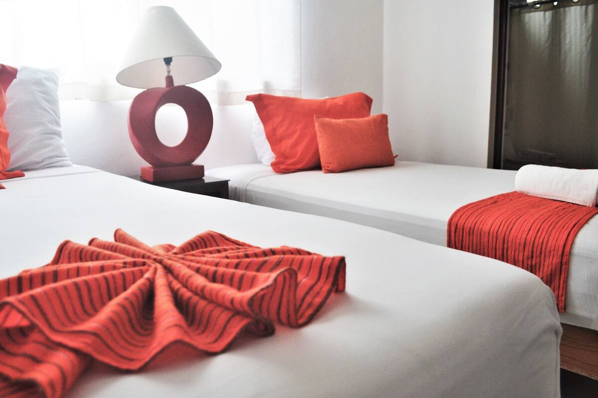 Habitación de hotel con dos camas, una lámpara roja y vistas a la ciudad.