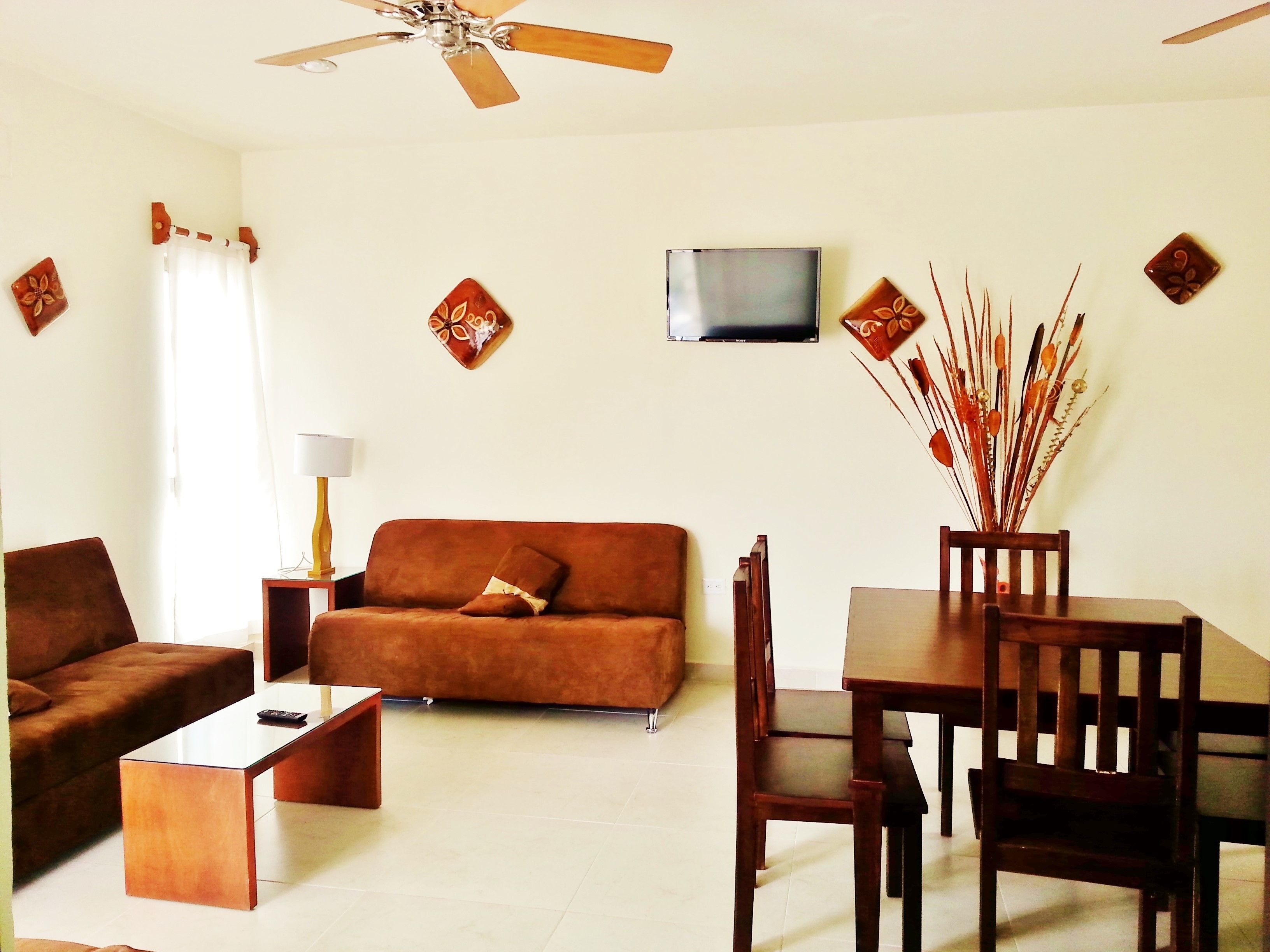 A living room with a sofa, coffee table, TV, and a dining area with chairs and a table.
