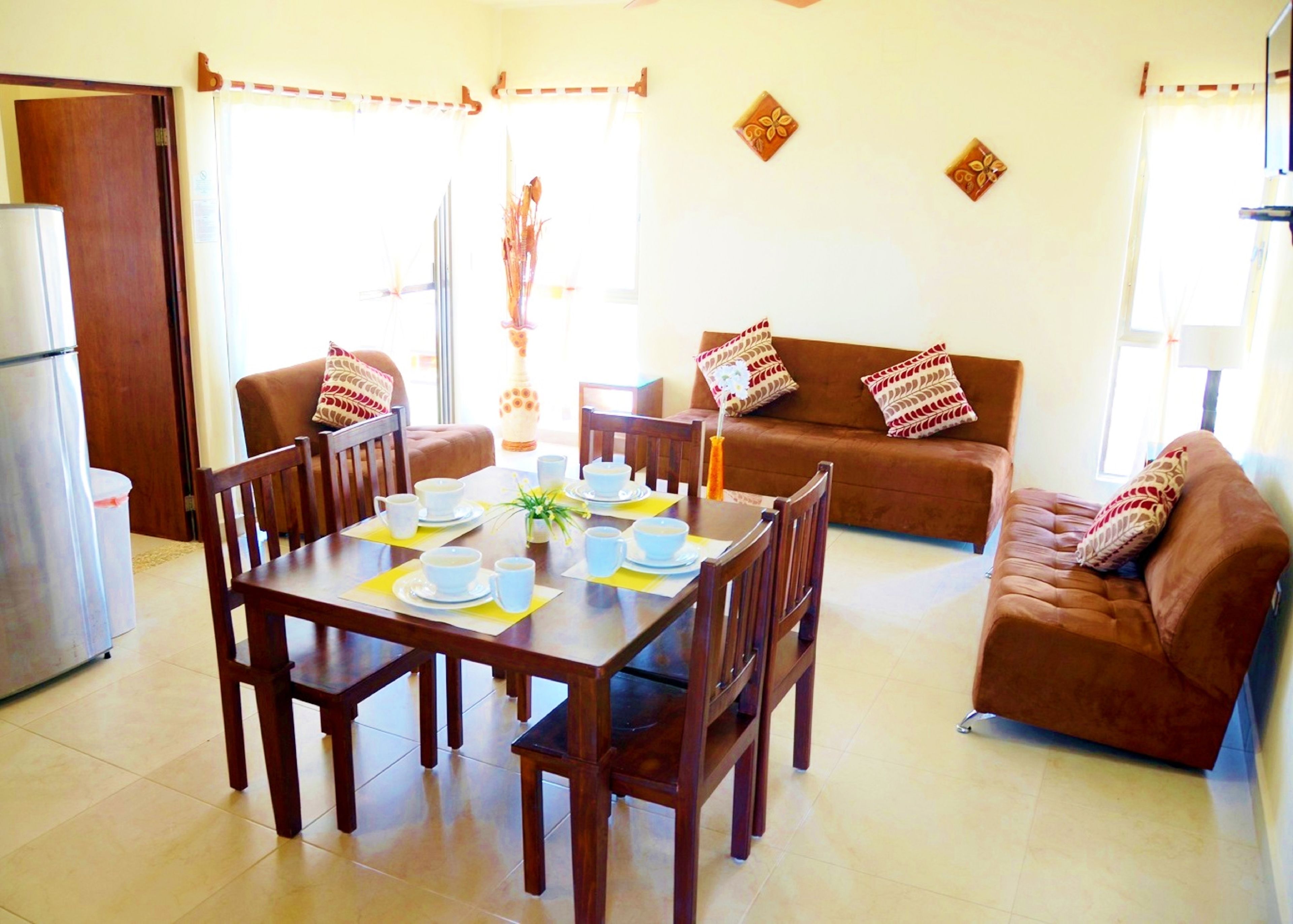 A dining area with a wooden table set for four, surrounded by brown sofas with patterned cushions.
