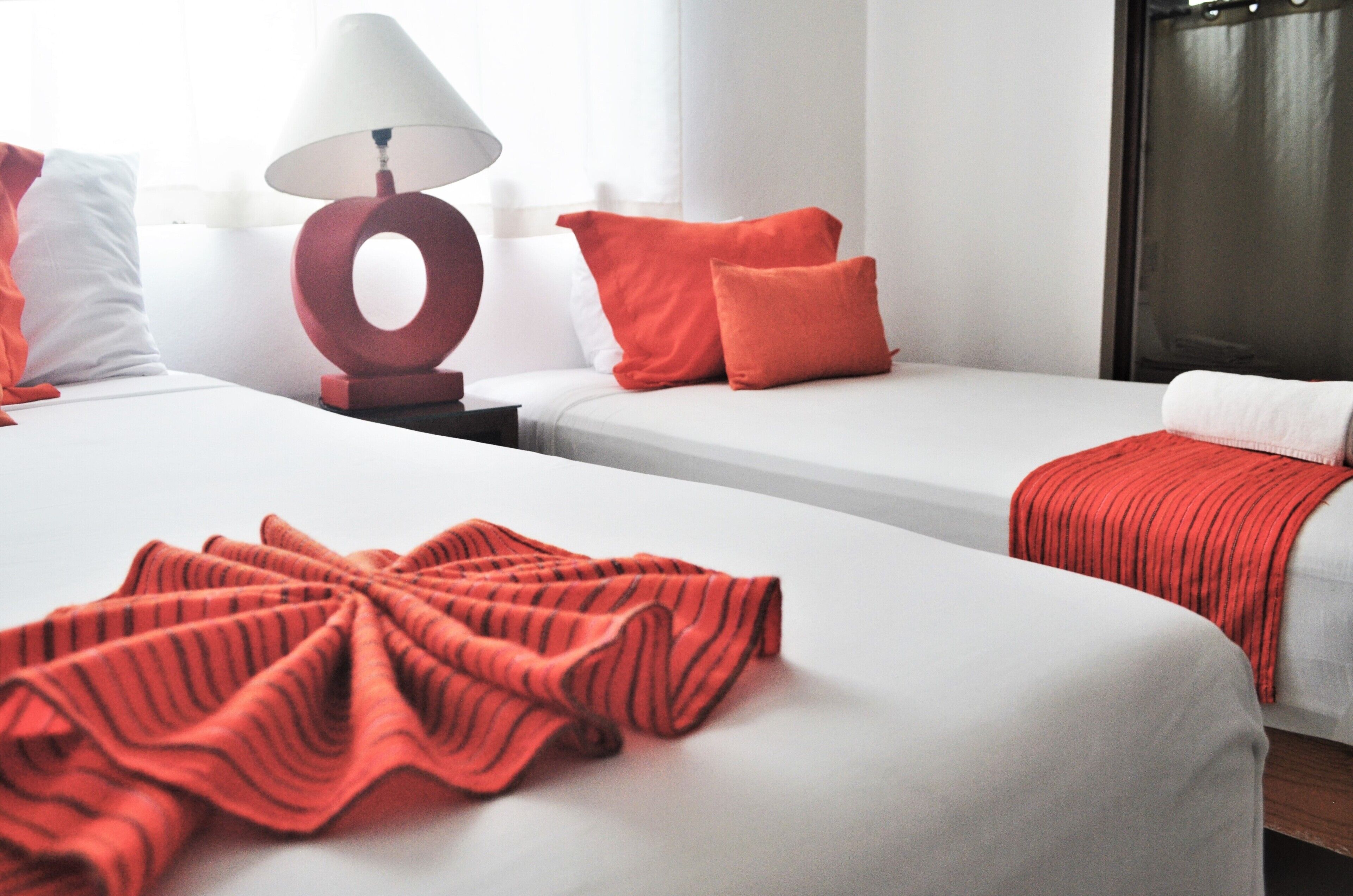 Quarto de hotel com duas camas, um abajur vermelho e vista para a cidade.