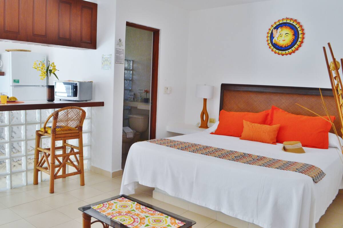 Una habitación de hotel con cama, escritorio, silla y baño visible a través de una puerta abierta.