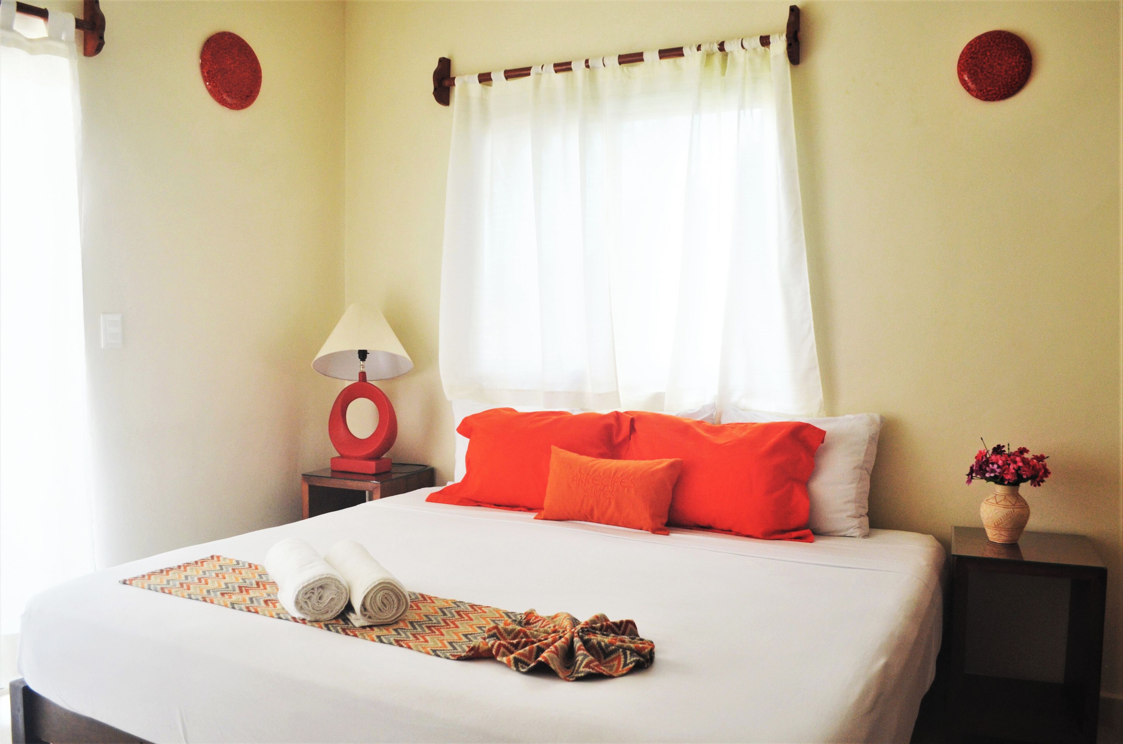 A neatly made bed with orange and white pillows, a rolled towel, and a patterned blanket.