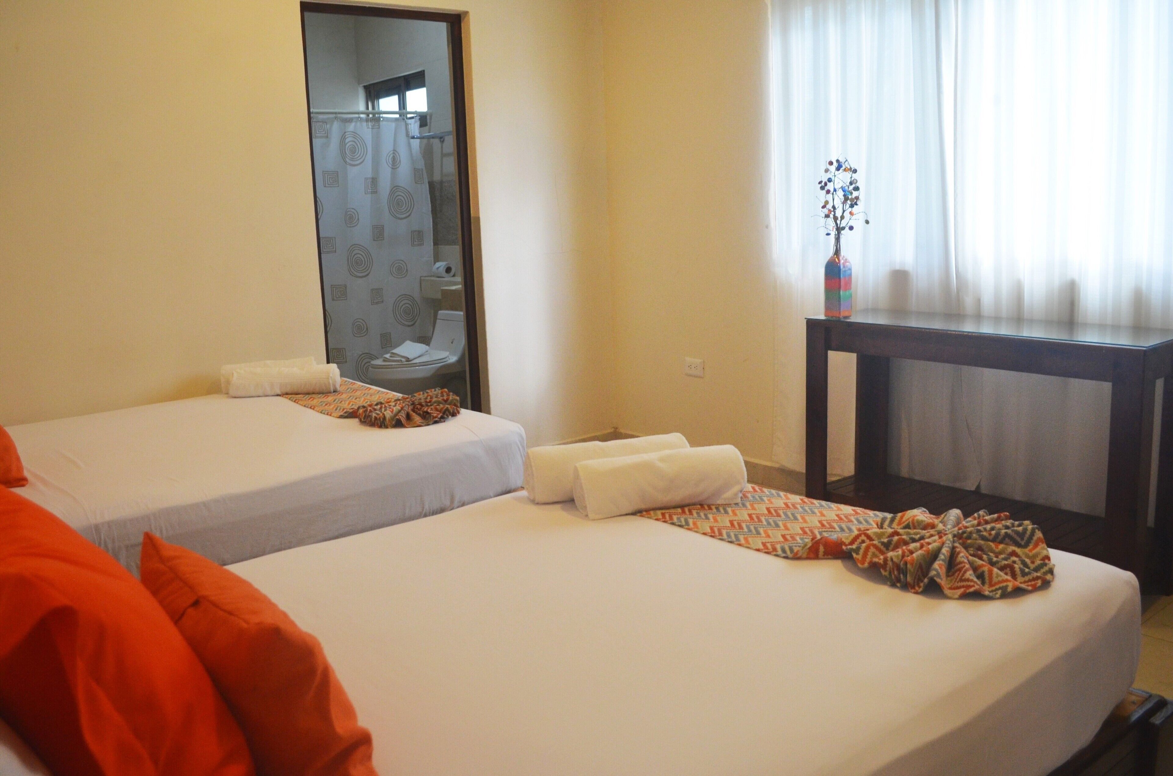 A hotel room with two beds, a small table, and a mirror.