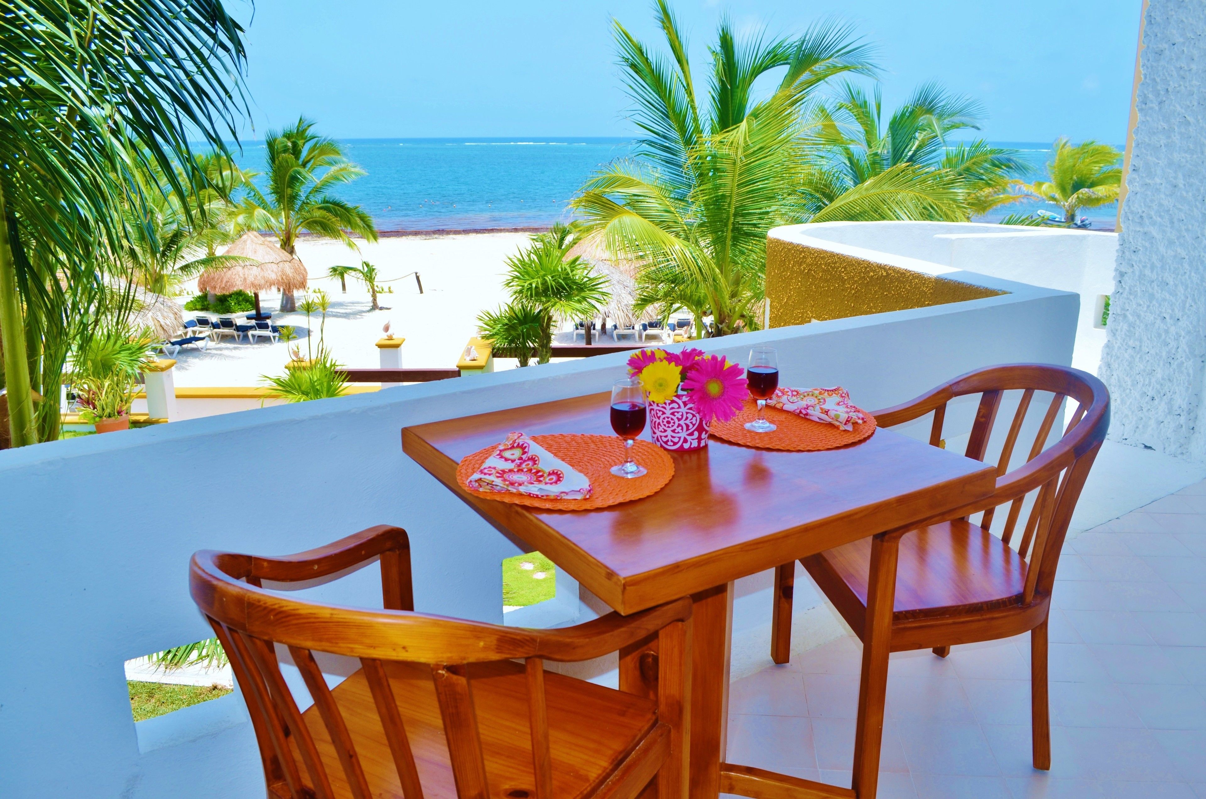 Une table en bois avec deux chaises, sur un balcon donnant sur une plage.