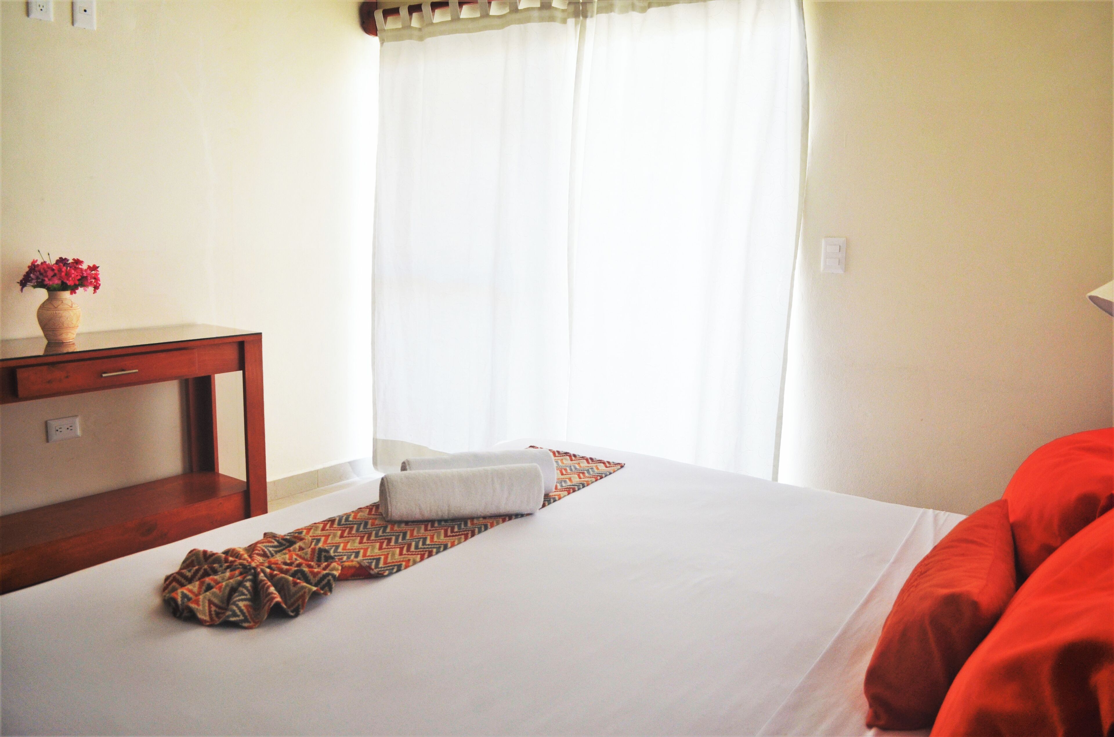 A hotel room with a bed, a desk, and a window with curtains.