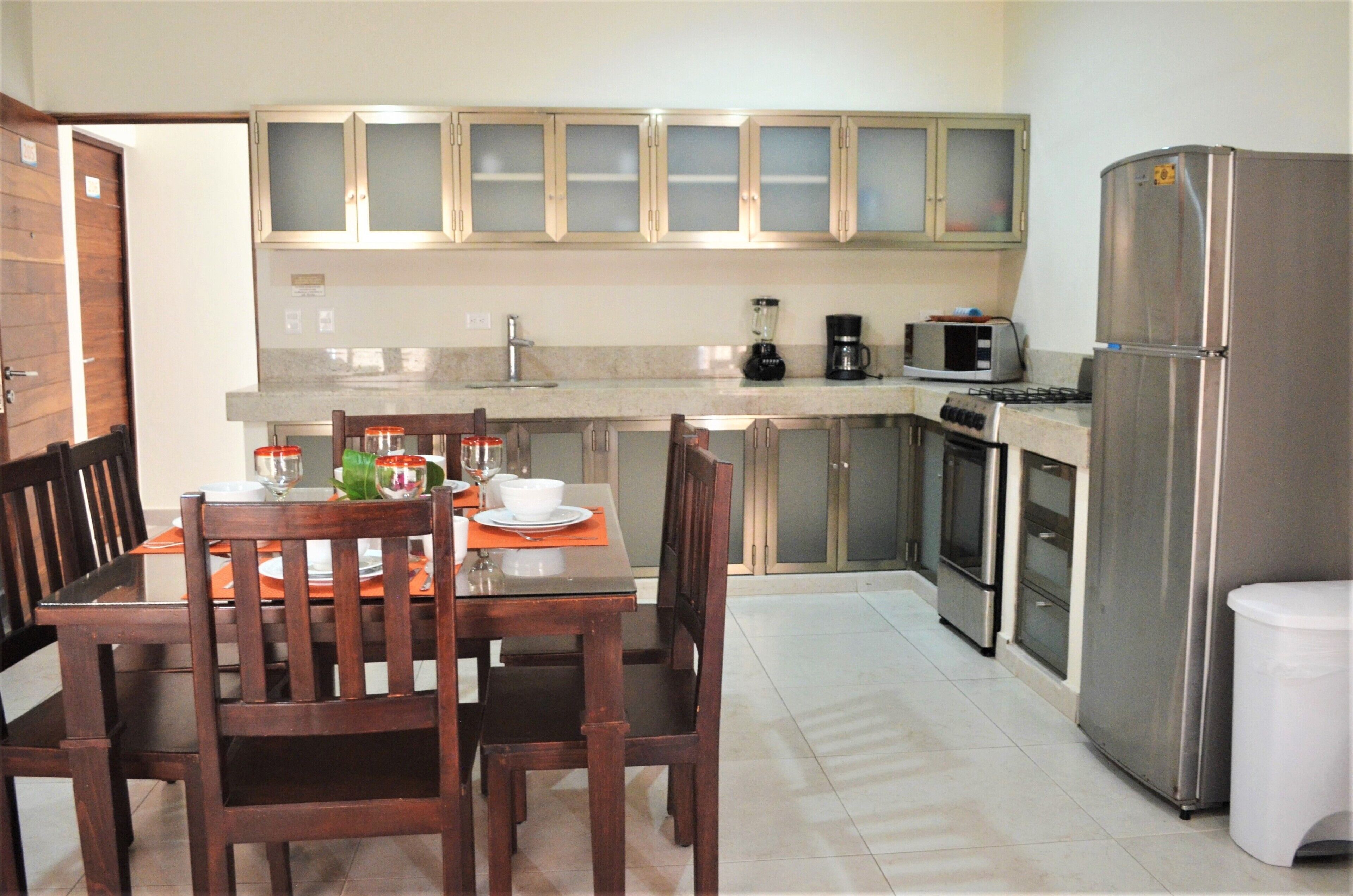 A kitchen with wooden cabinets, a stainless steel refrigerator, and a dining table with chairs.