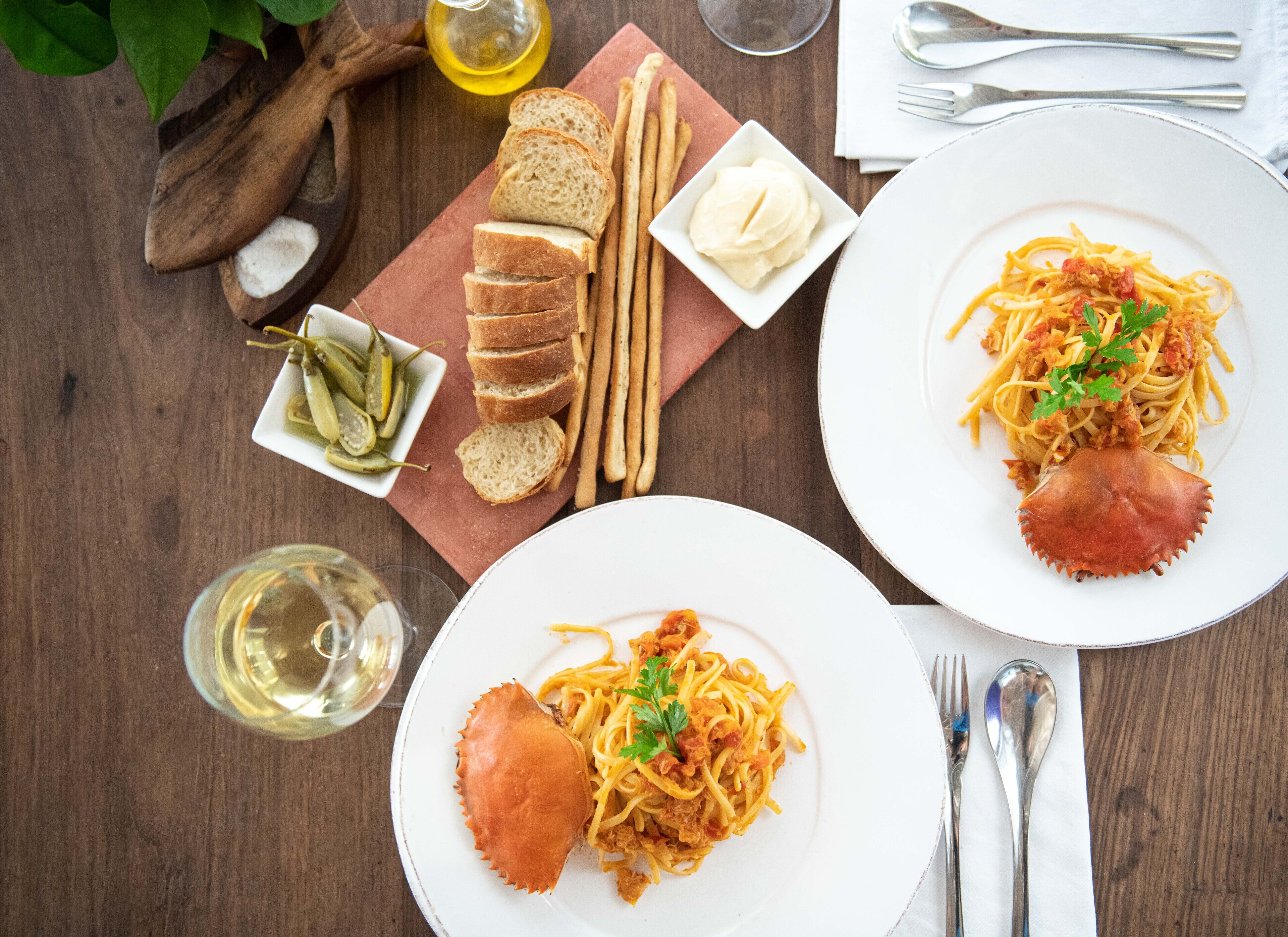Een eettafel met borden spaghetti, broodstengels en augurken. Ook staan er glazen wijn en bestek bij.