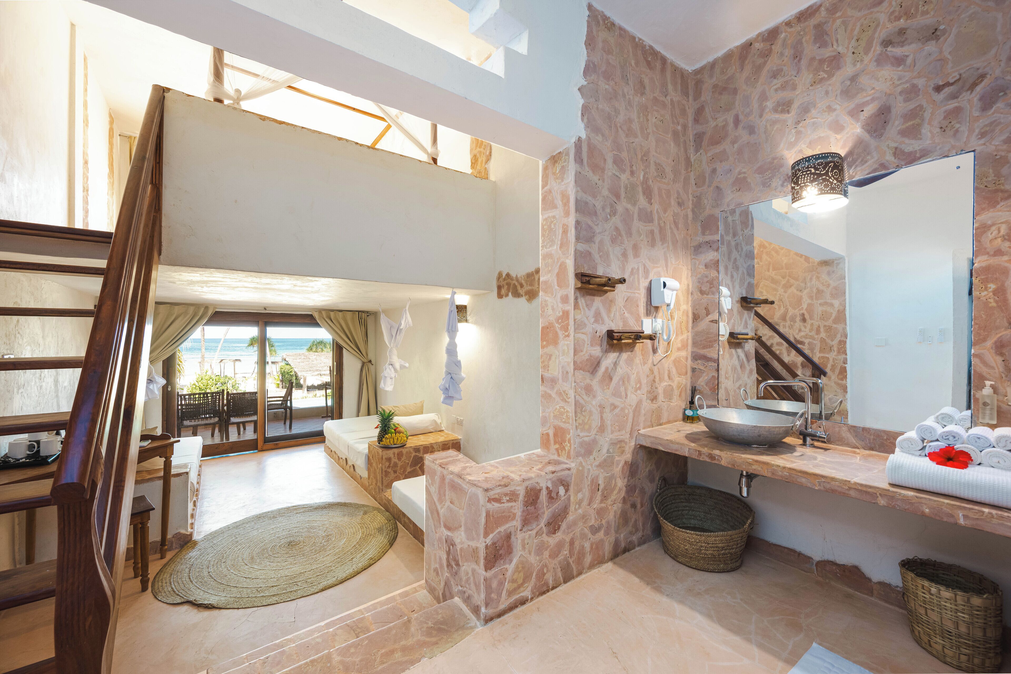 A spacious bathroom with a stone wall, a large mirror, and a sink with towels.