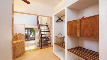 A hallway with a wooden staircase, a stone wall, and a wooden cabinet with a hanging garment.