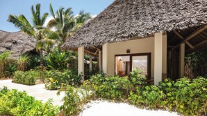 A thatched-roof building with a door and windows, surrounded by lush greenery and palm trees. - Mvuvi Boutique Resort (Kiwengwa)