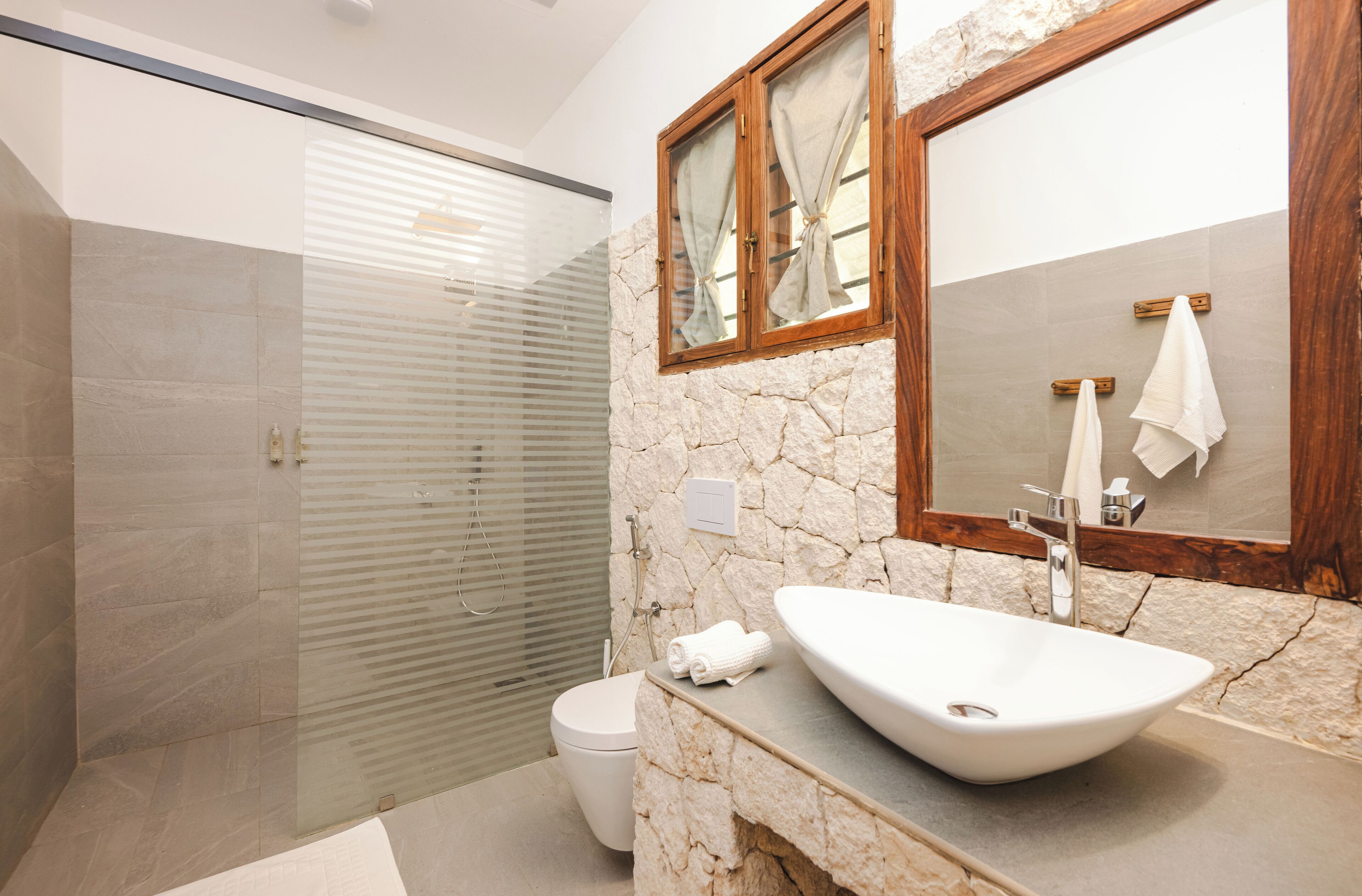 Un baño moderno con pared de piedra, un lavabo grande y cabina de ducha de vidrio.