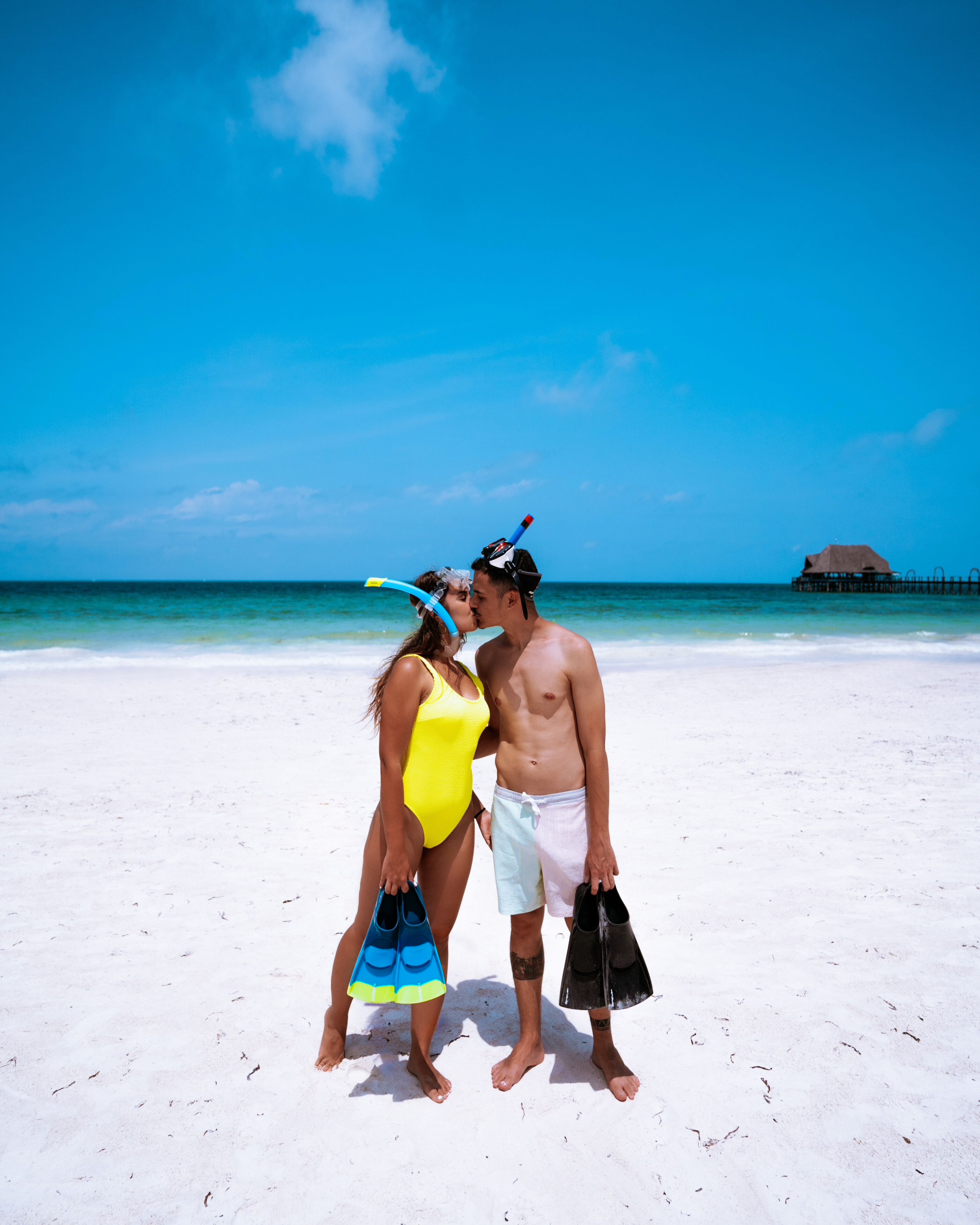 A couple on a beach with clear skies and ocean in the background.