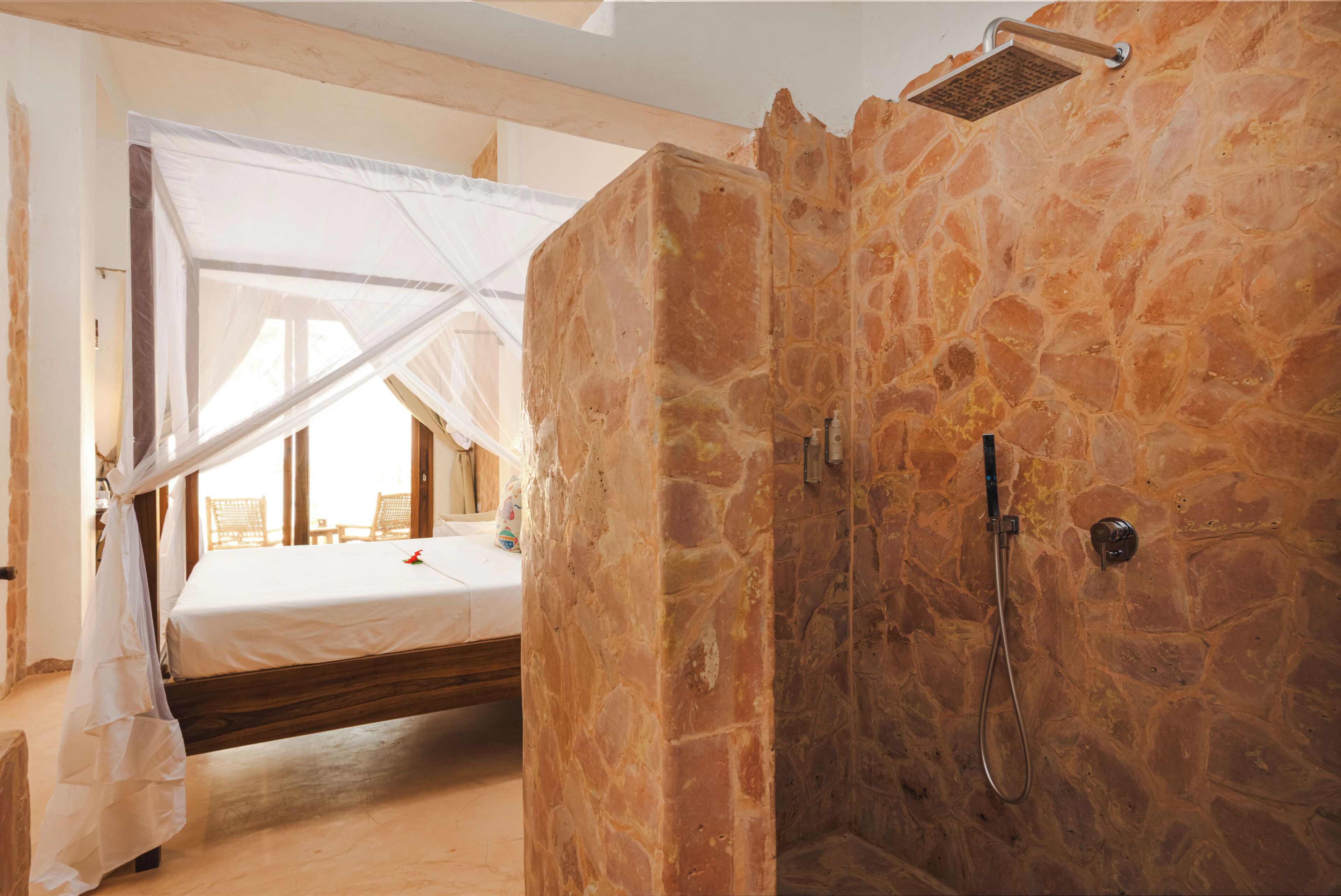 Une chambre avec une douche en pierre, un lit à baldaquin et une vue sur l’extérieur.