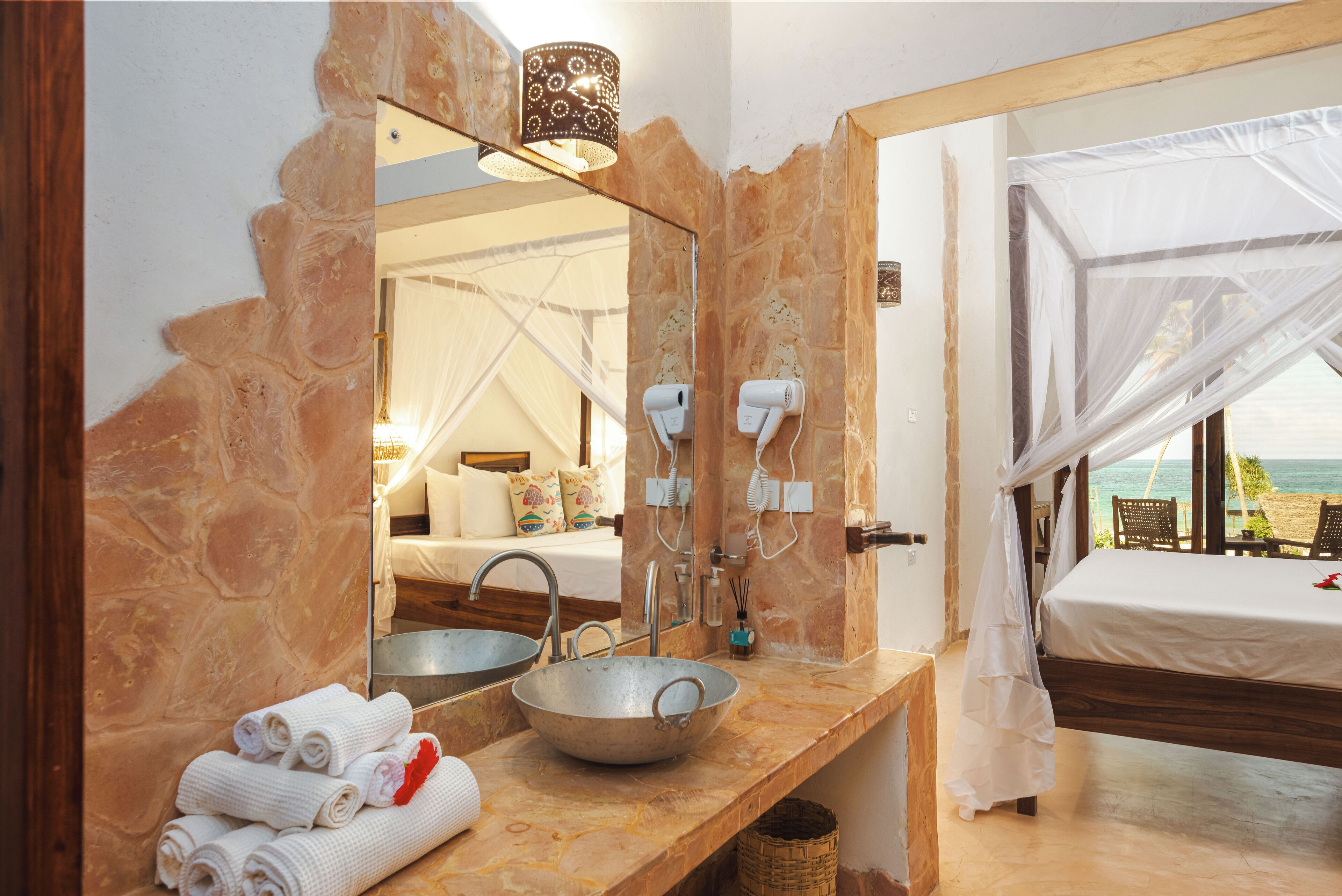 Une salle de bain avec un mur en pierre, un grand miroir, un lavabo et un lit à baldaquin.