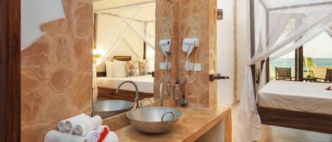 A bathroom with a stone wall, a large mirror, a sink, and a bed with a canopy.
