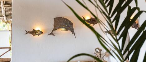 A dining area with a wooden table set for two, a sofa with blue cushions, and a wall with fish-shaped wall art.