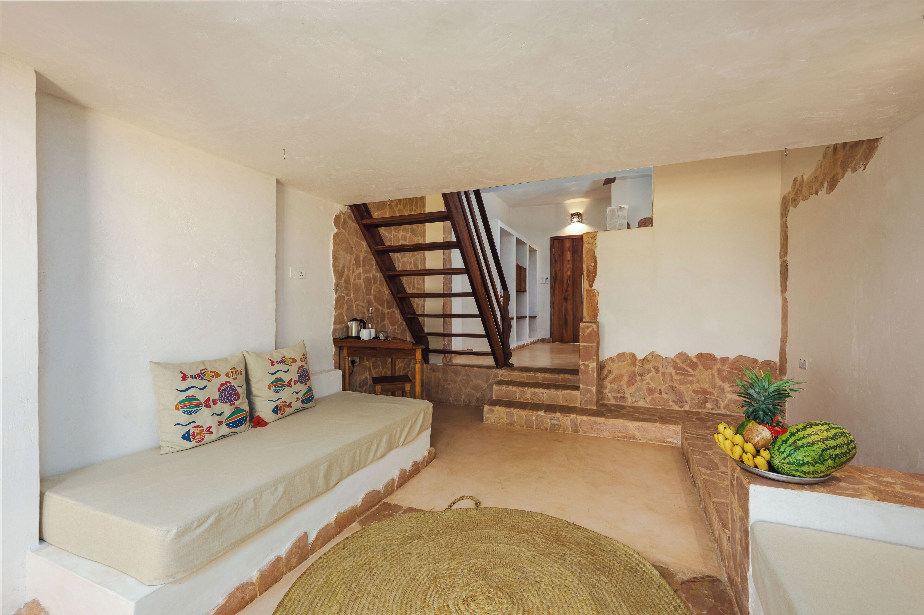 Une pièce chaleureuse avec un canapé, un tapis tissé, un panier de fruits et un escalier menant à un autre espace.