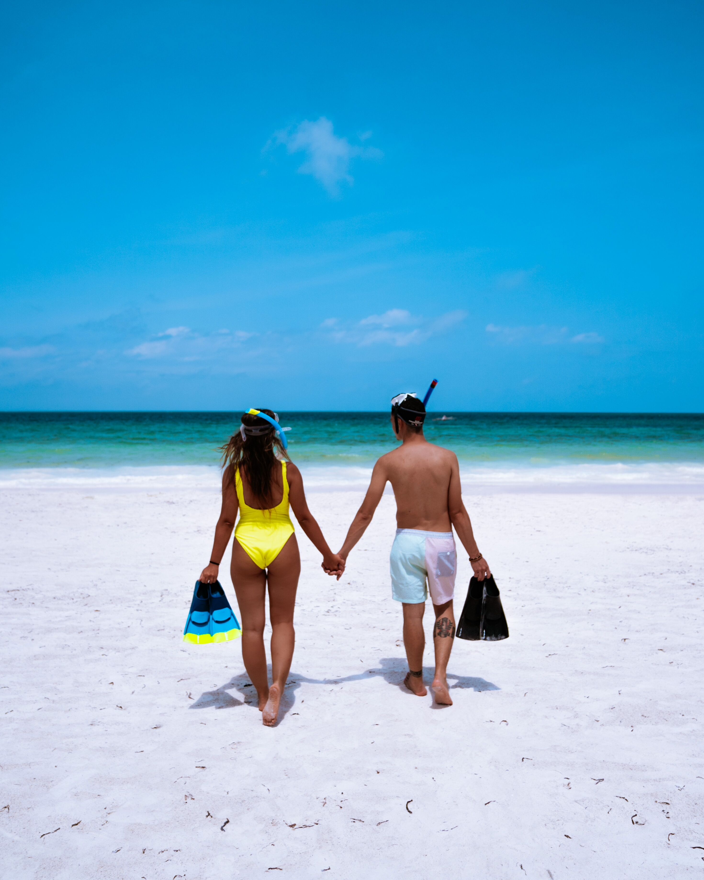 A couple walking on a sandy beach with the ocean in the background.