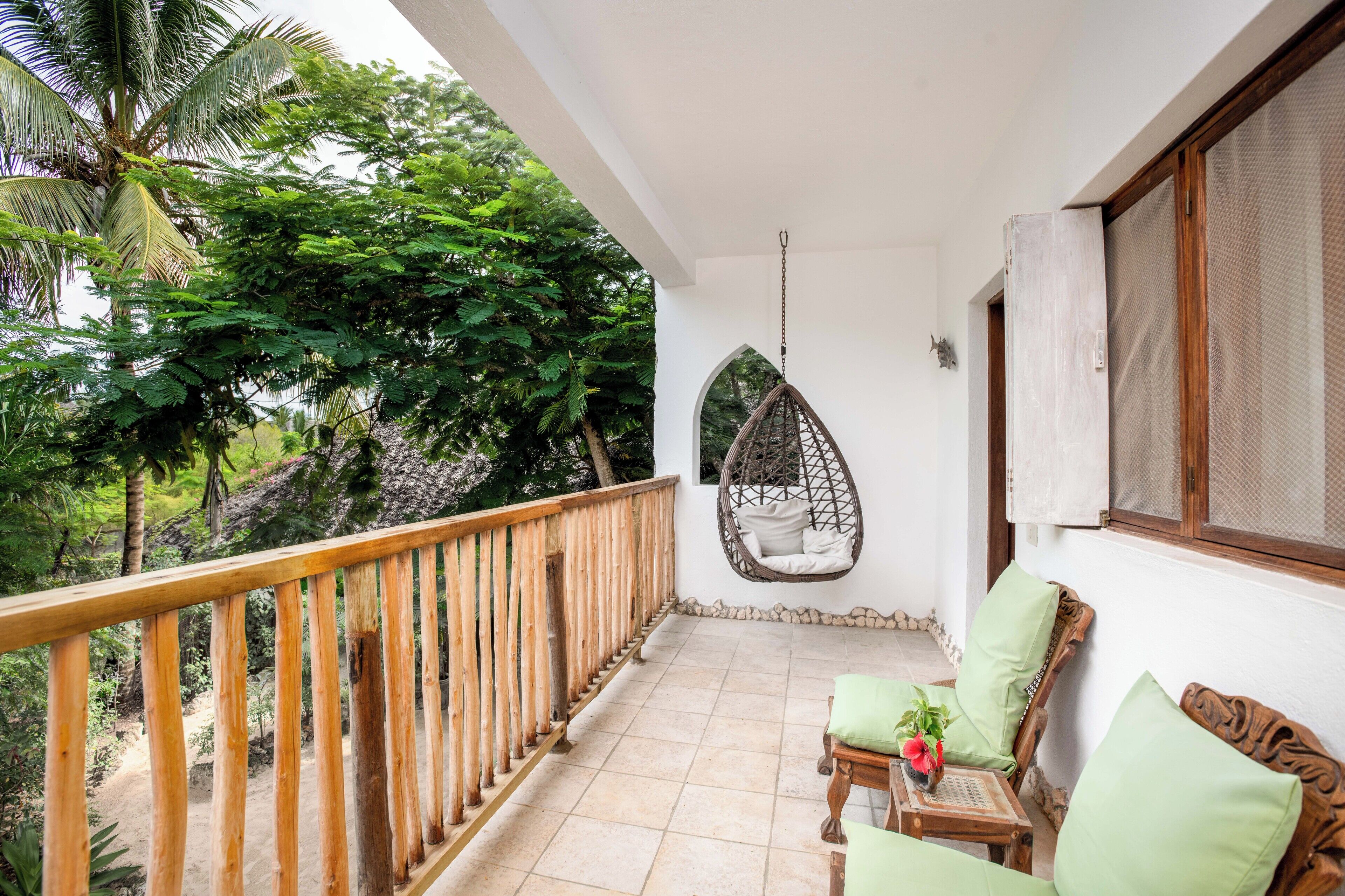 Un balcon agrémenté d’un fauteuil suspendu, de meubles en bois et offrant une vue sur une végétation luxuriante.