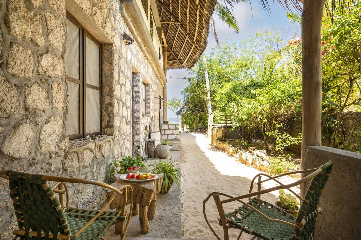 Un bâtiment en pierre doté d’un patio avec un toit de chaume, d’un espace extérieur aménagé pour s’asseoir et offrant une vue sur la plage.