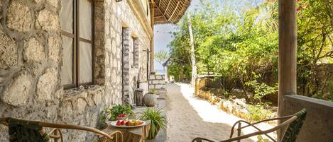 Edificio de piedra con techo de paja, patio, asientos al aire libre y vista a la playa.