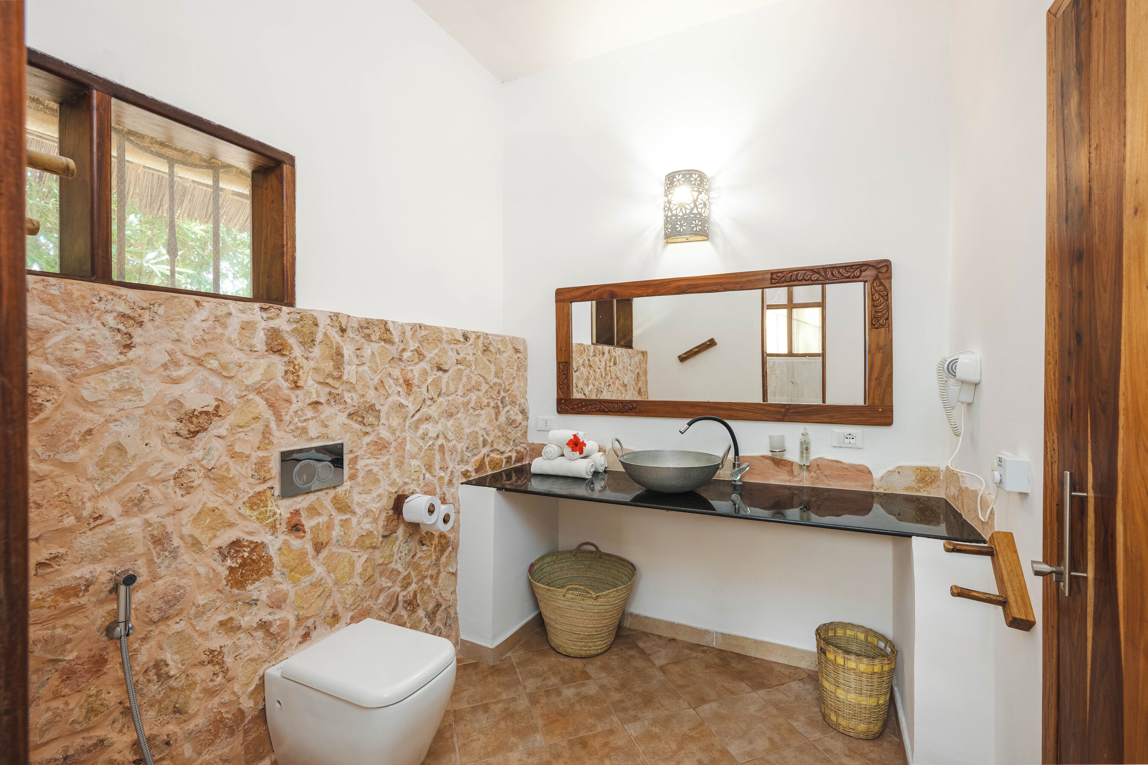 Un baño con pared de piedra, lavamanos de cristal, puerta de madera y un espejo.