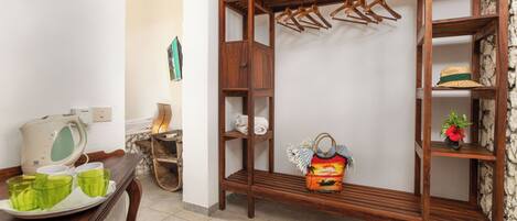 A room with a wooden wardrobe, a bench, a tray with green cups, and a hanging rack with clothes.