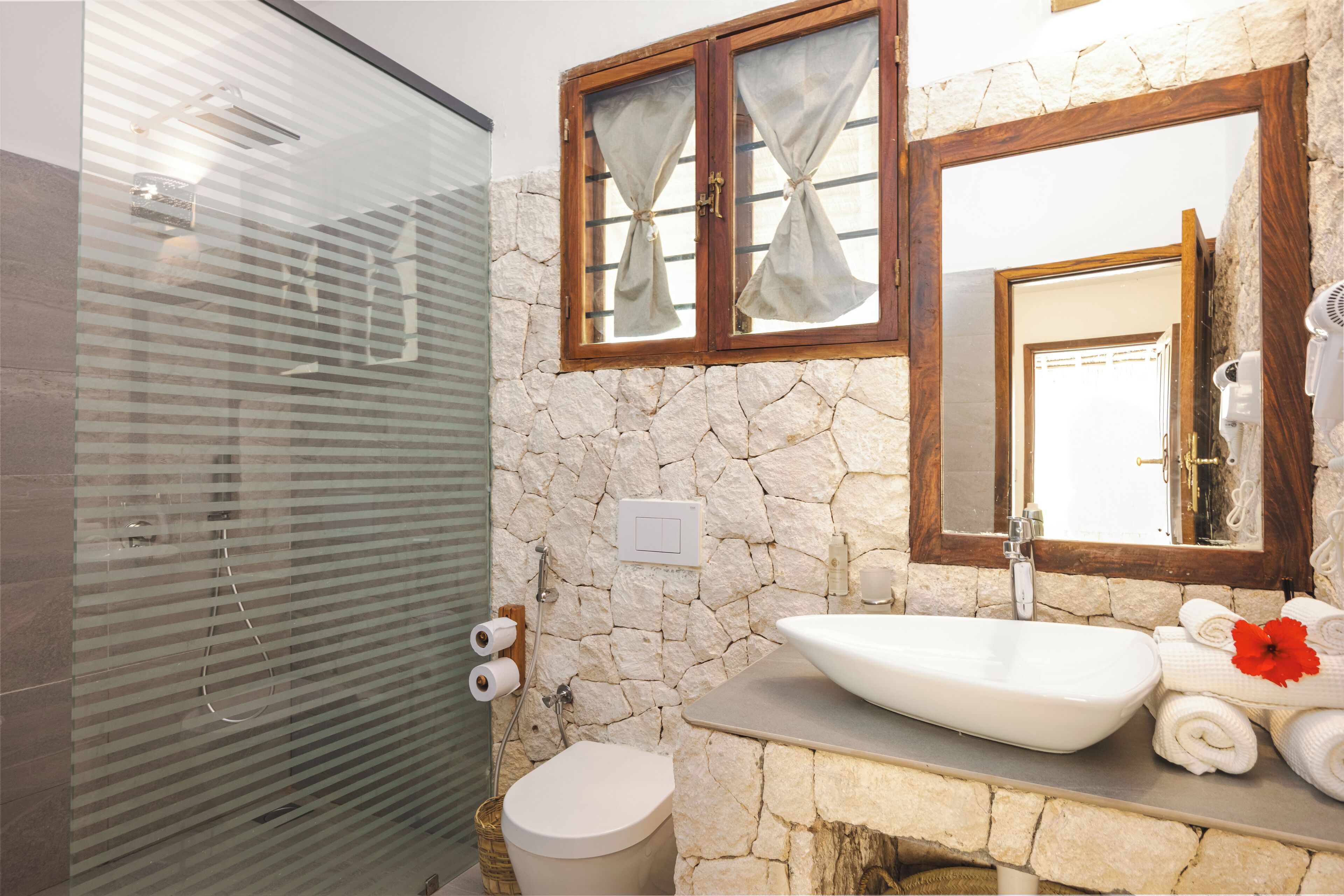 Ein Badezimmer mit Steinwand, Waschbecken, Spiegel und Dusche.