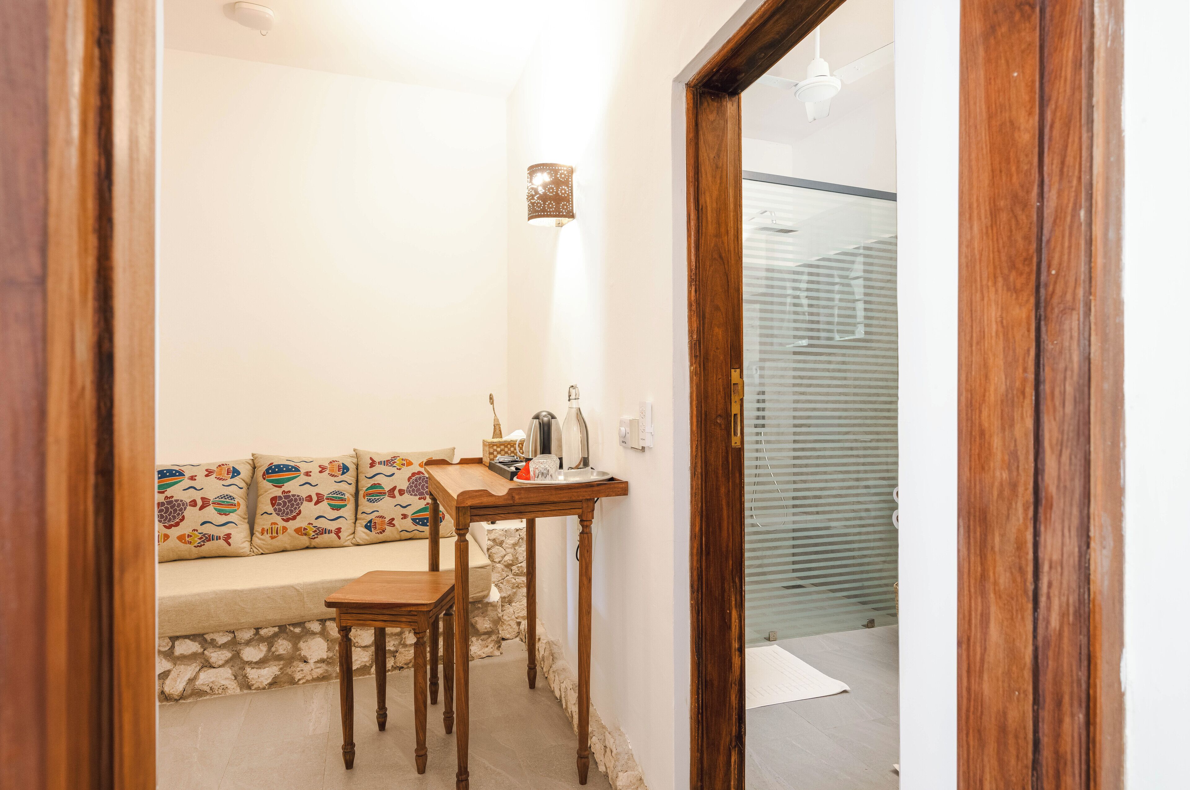 Una habitación acogedora con una mesa de madera, un banco con cojines coloridos y una lámpara fijada a la pared.