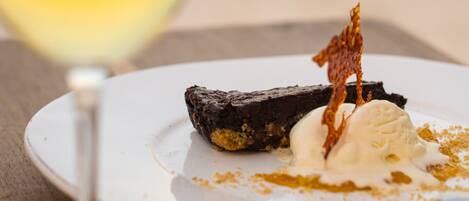 A dessert plate with a piece of cake and ice cream, accompanied by a glass of white wine, on a table with a blurred background.