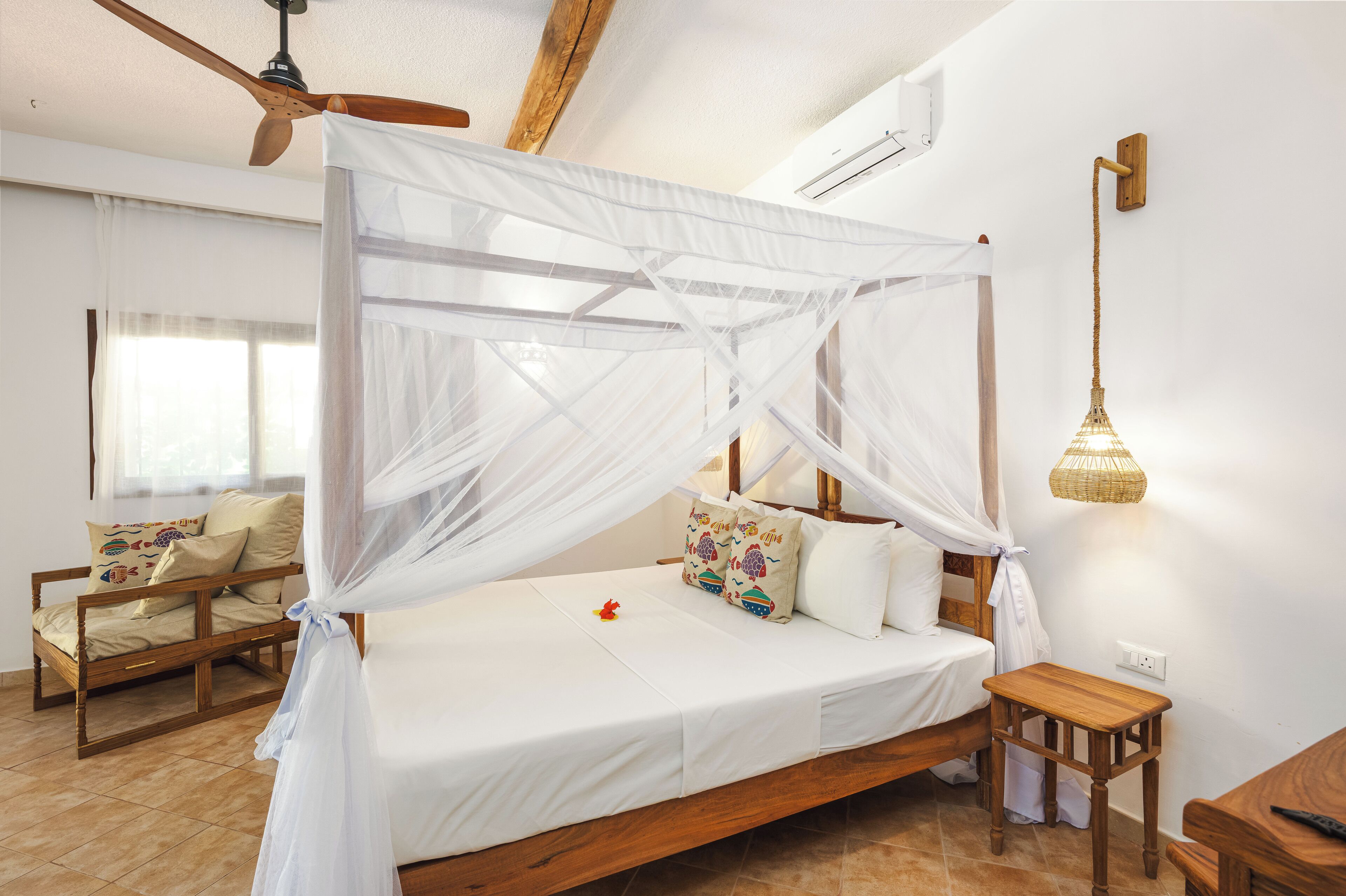 Een slaapkamer met een bed met witte hemel, een houten stoel, een klein tafeltje en een hanglamp.