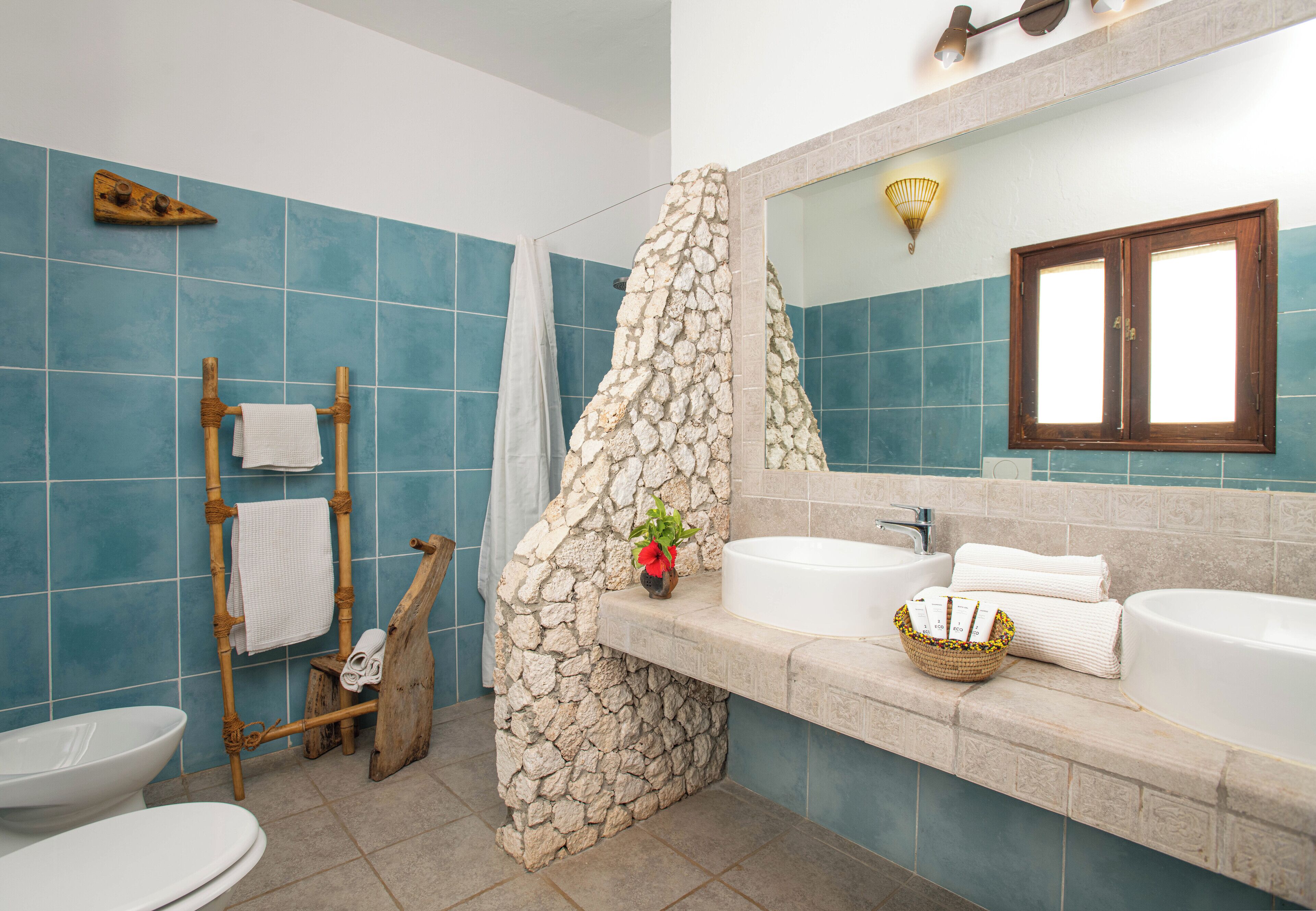 Un baño con cabina de ducha de piedra, toallero de madera, lavabo blanco y un espejo grande.