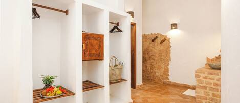 A hallway with white walls, wooden shelves, and a stone wall.