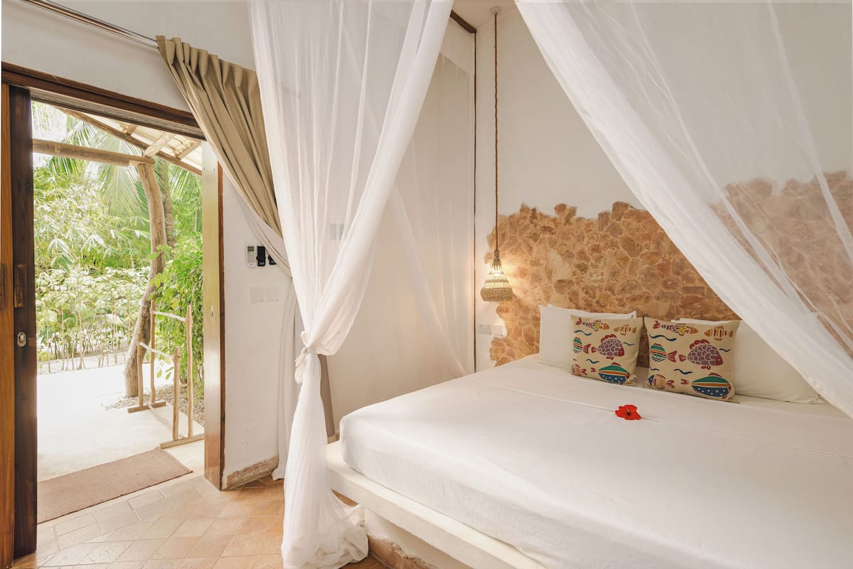 Une chambre à coucher avec une tête de lit en pierre, un lit recouvert de linge de lit blanc et une vue sur la verdure, visible à travers une porte vitrée.