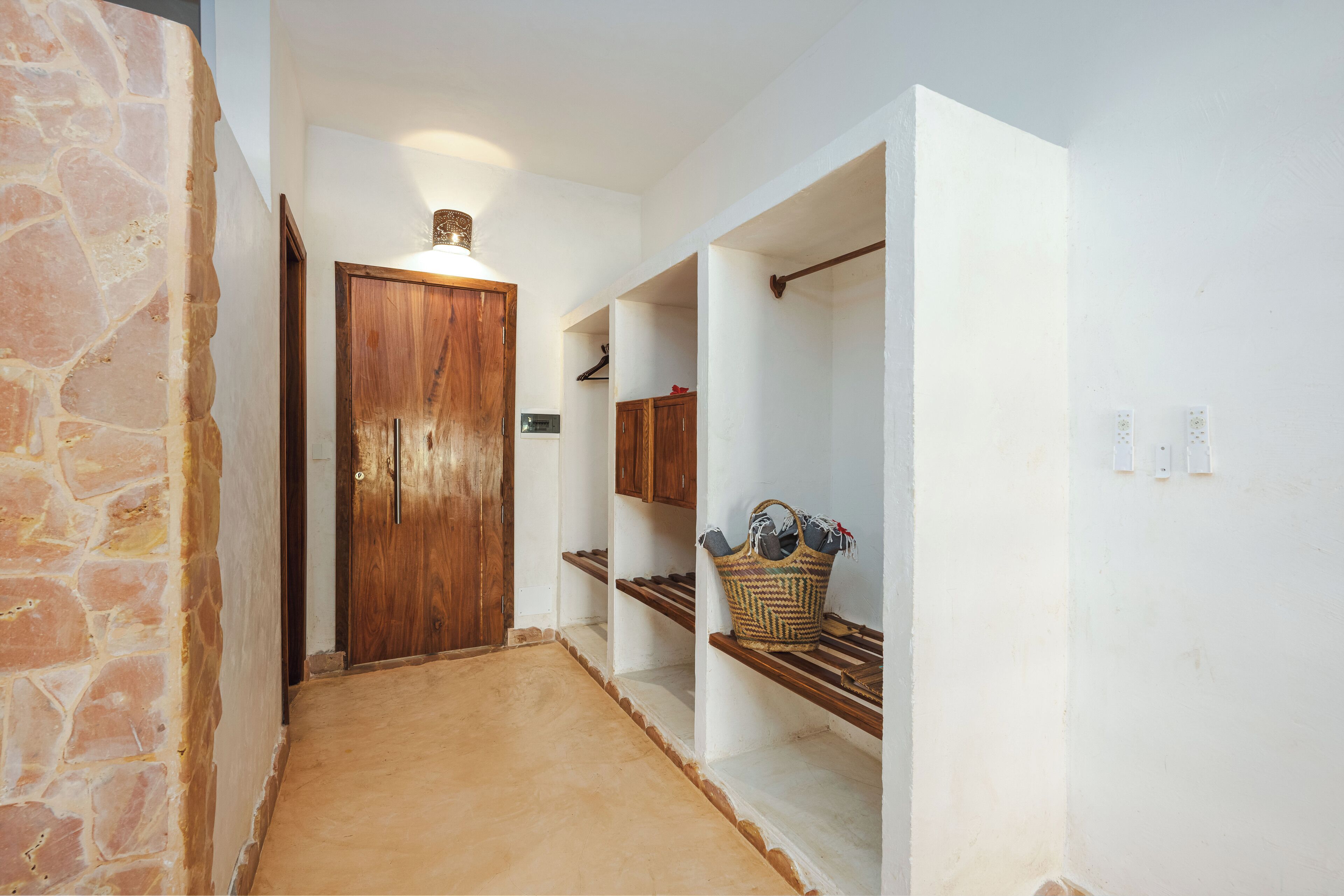 A hallway with a stone wall, a wooden door, and shelves with baskets.