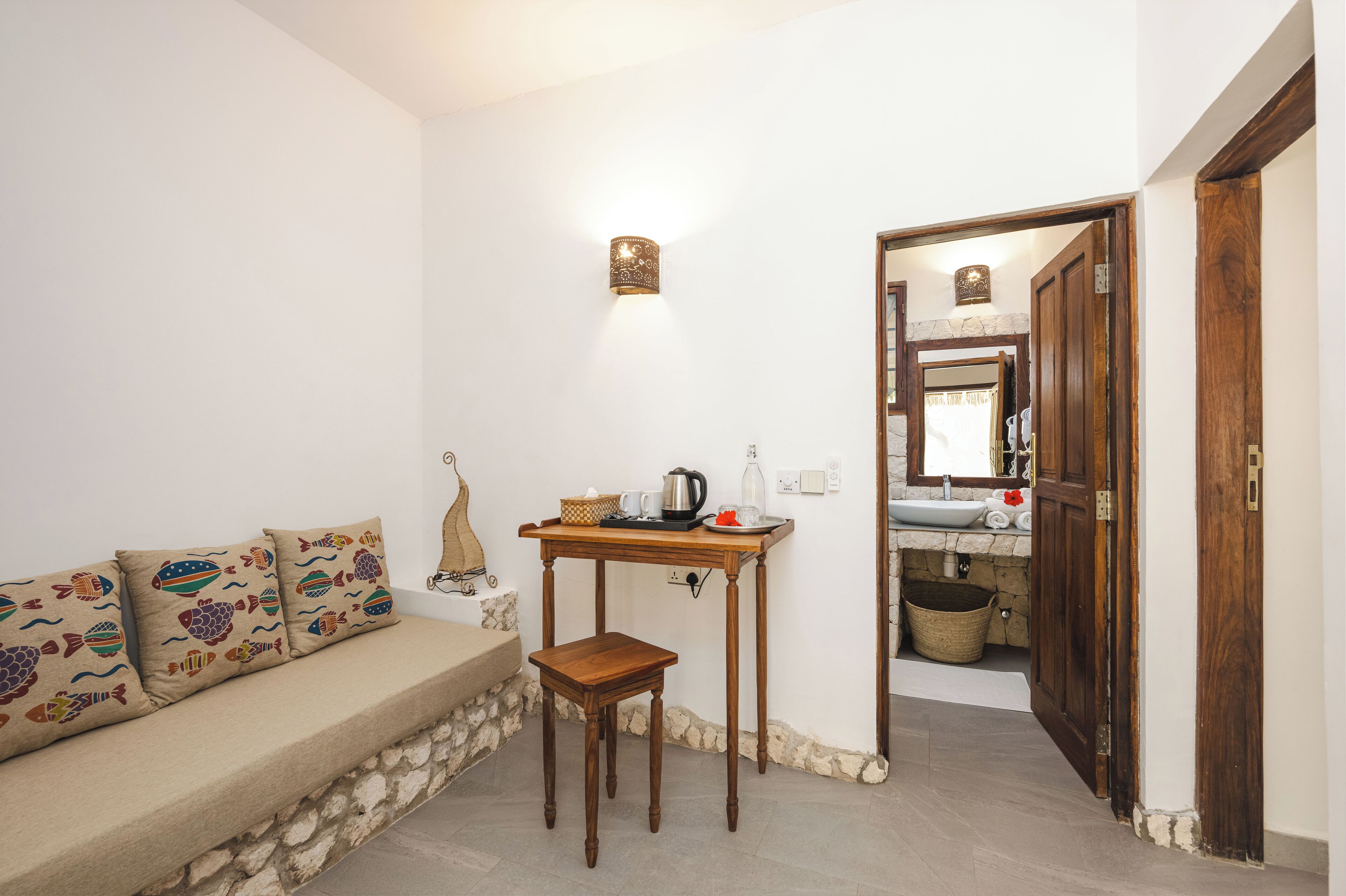 A cozy room with a sofa, a small wooden table with a kettle, and a doorway leading to a bathroom.