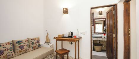 A cozy room with a sofa, a small wooden table with a kettle, and a doorway leading to a bathroom.