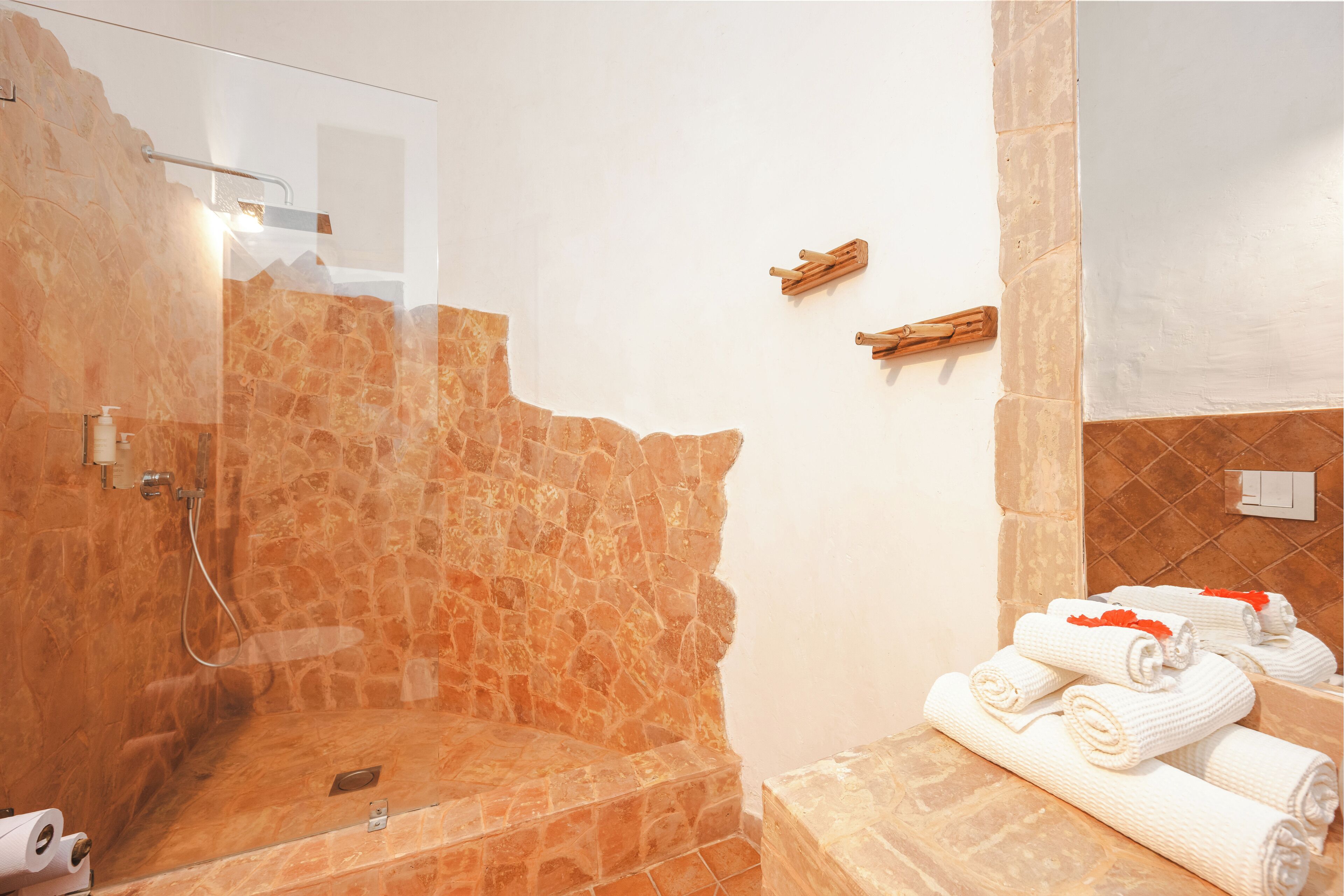 Een badkamer met een stenen douche, een wastafel met spiegel en handdoeken op een aanrecht.