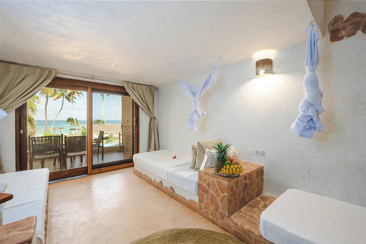 Une chambre avec un lit, une petite table sur laquelle se trouvent des fruits, un banc et une vue sur la plage.