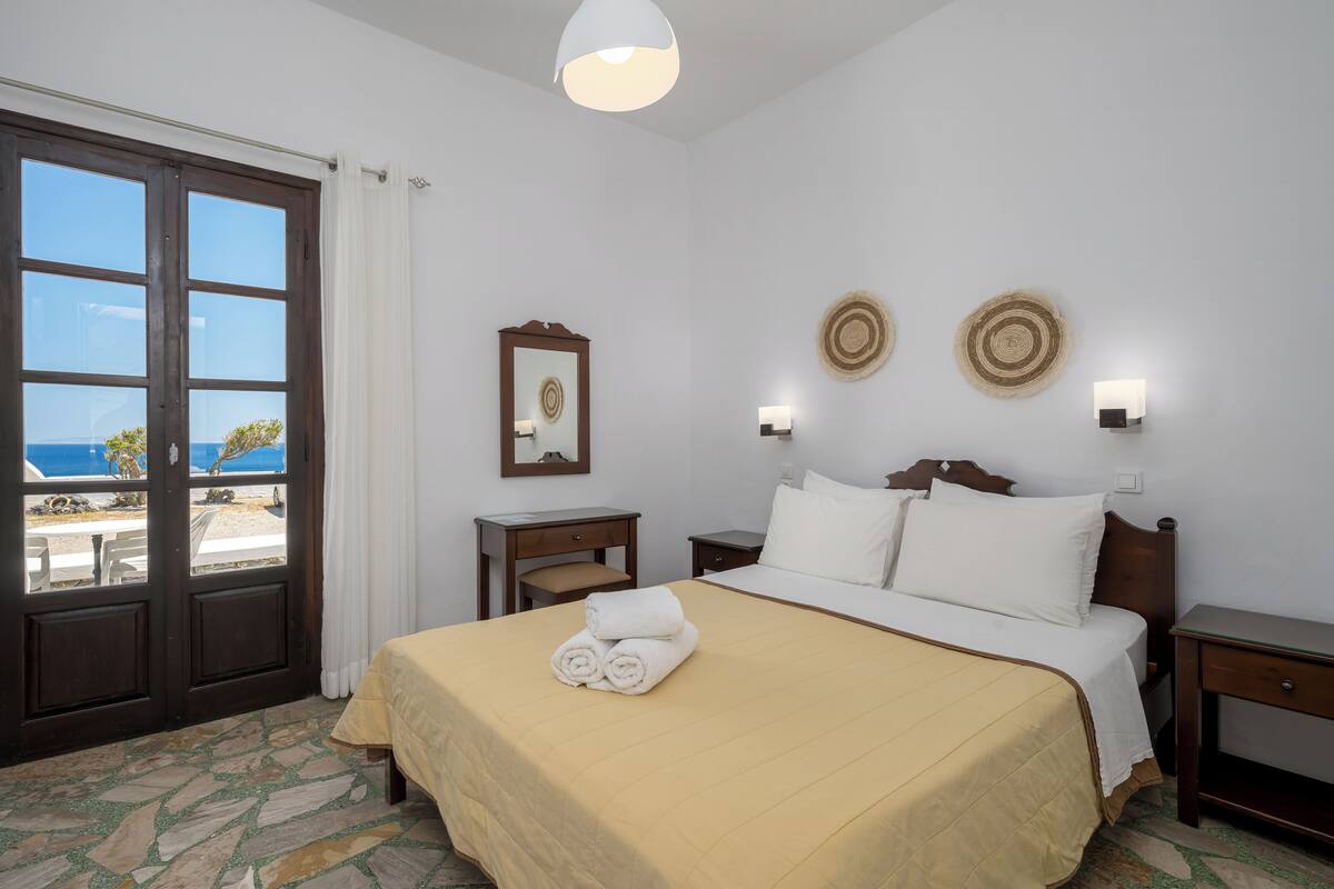 A hotel room with a bed, a desk, a chair, a mirror, and a view of the sea.