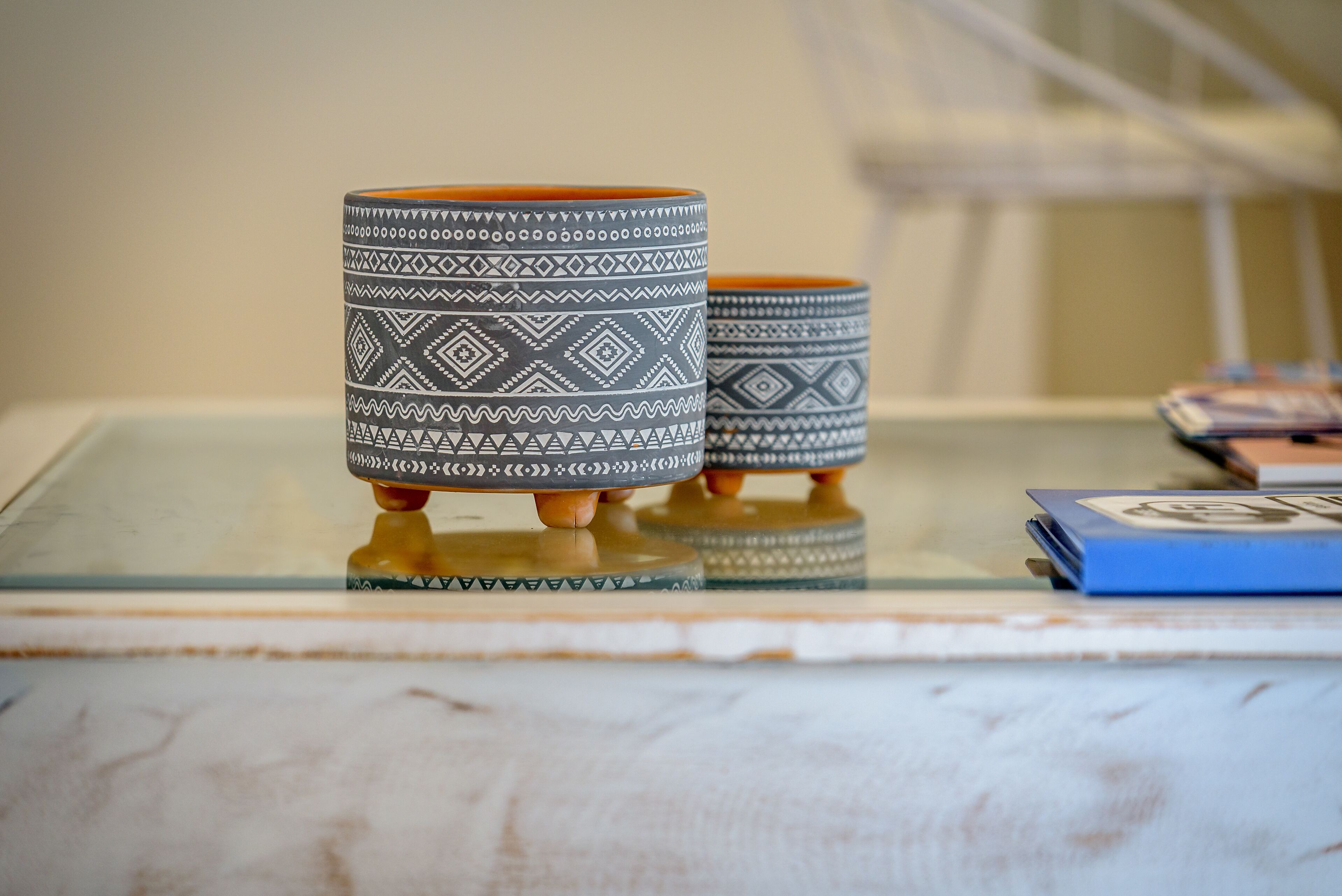 Two patterned ceramic cups on a glass table with a blue book beside them.