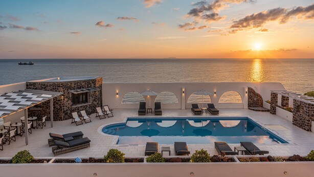 A poolside area with lounge chairs and umbrellas, overlooking the sea at sunset. - Agia Irini (Santorini)