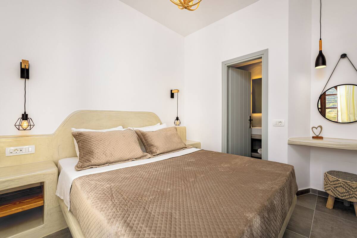 A bedroom with a bed, bedside lamps, a bedside table, a mirror, and a small stool.