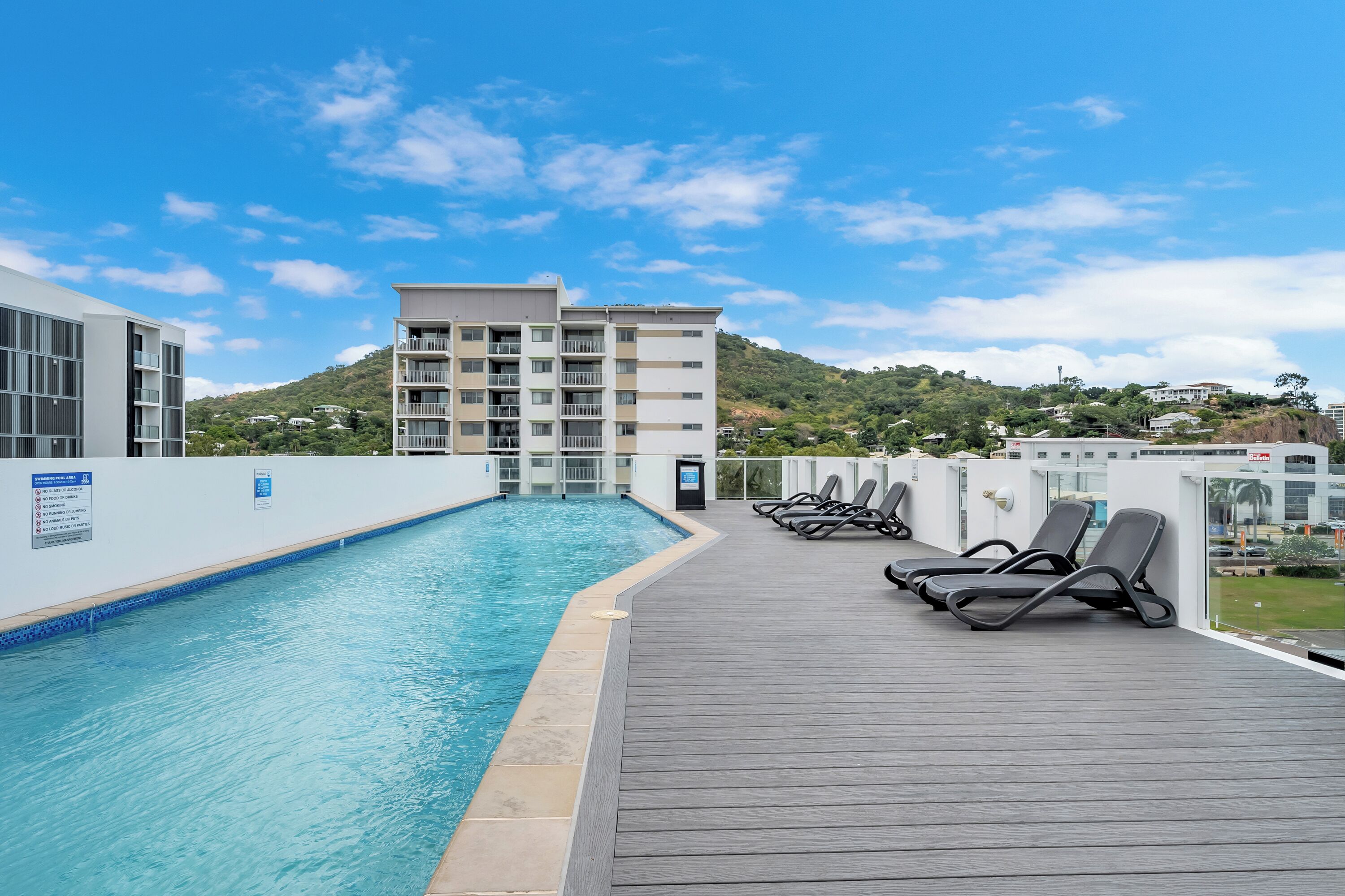 A rooftop pool with lounge chairs, a view of a hillside, and a modern building in the background.